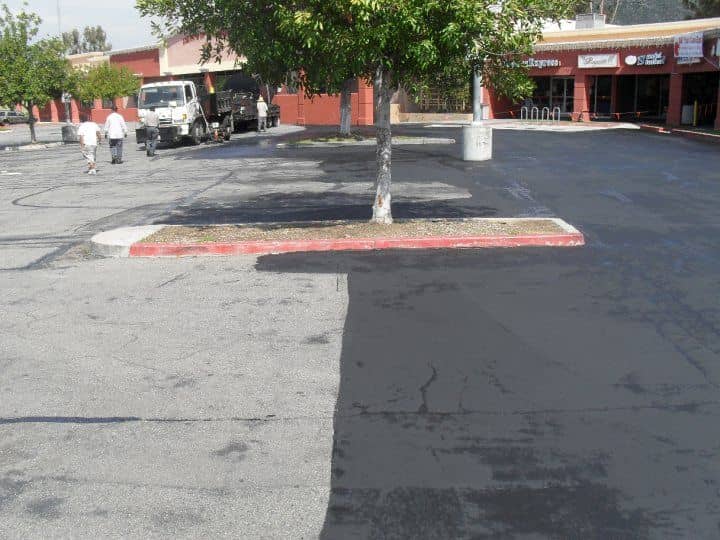 MGB project photo: one parking area split down the middle, weathered gray asphalt on the left and fresh black sealcoat on the right