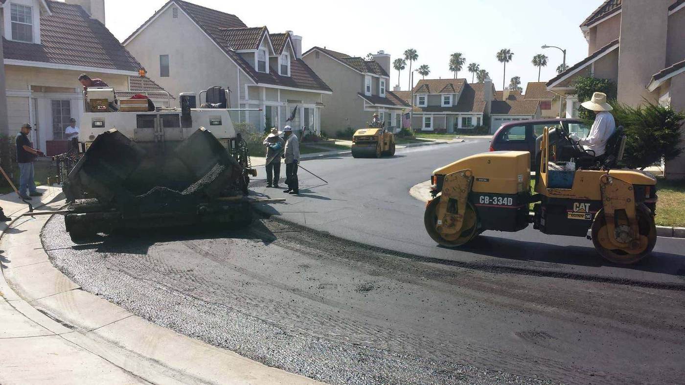 MGB paver laying a new asphalt mat on a residential street in Santa Ana, roller compacting behind it